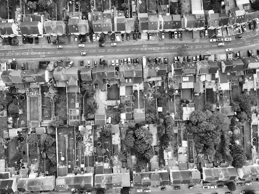 An aerial view of a residential neighborhood featuring a variety of gardens, lawns, and landscaped areas. The scene shows multiple houses with well-maintained front and back gardens, some with trimmed